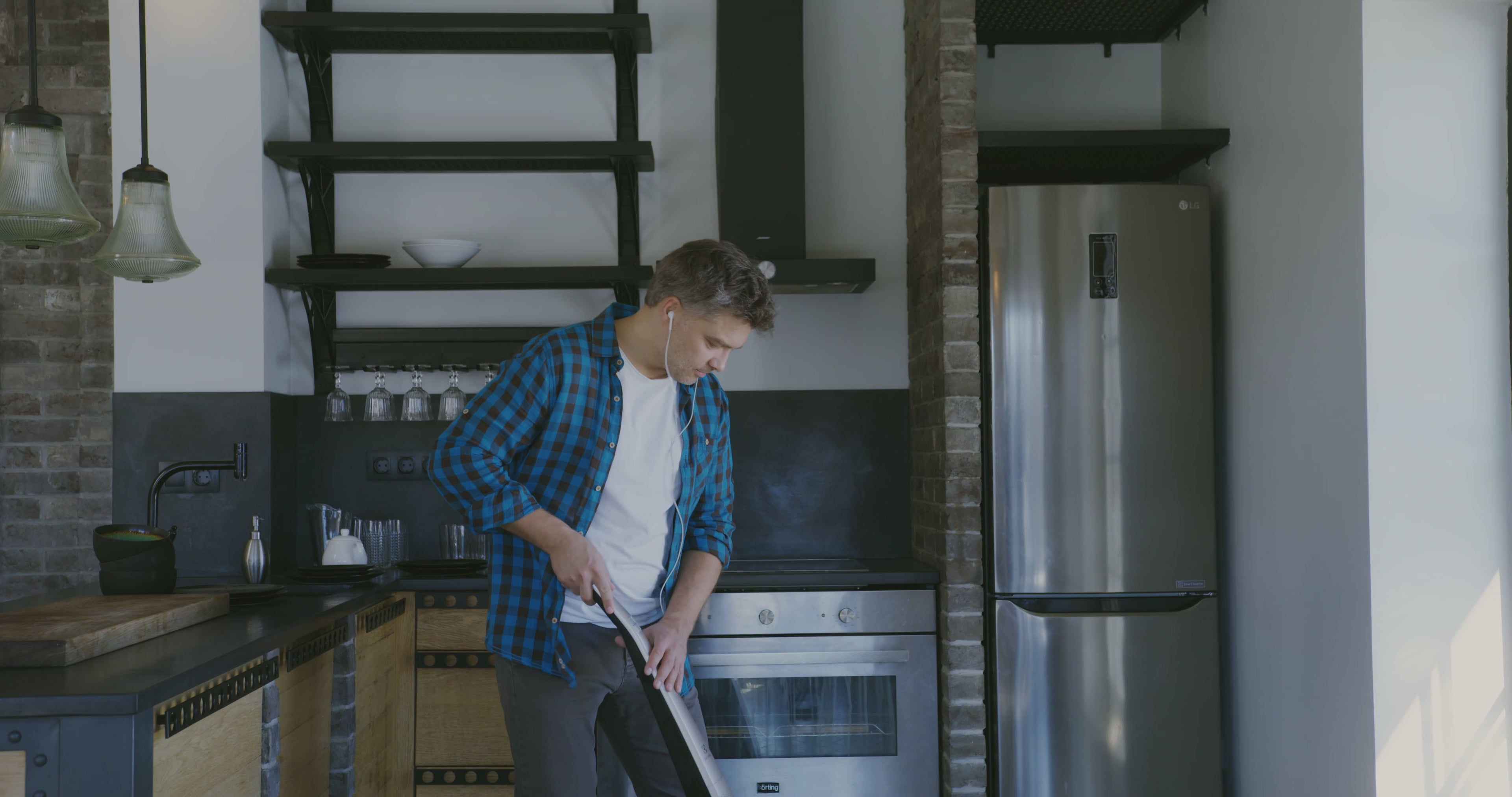 Cargar video: Hombre bailando y disfrutando música mientras limpia la cocina con ayuda de un dispositivo tecnológico, mostrando cómo las tareas del hogar pueden ser más fáciles y divertidas.